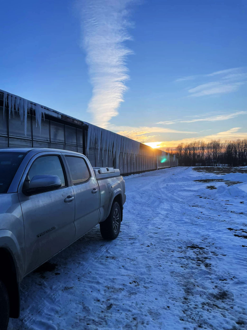 truck parked in the snow by a barn at sunset