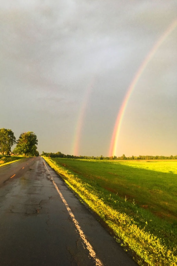 double rainbow over a field by a road